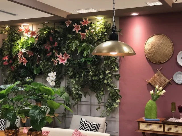 Parede verde com flores, candeeiro e mobiliário da mostra