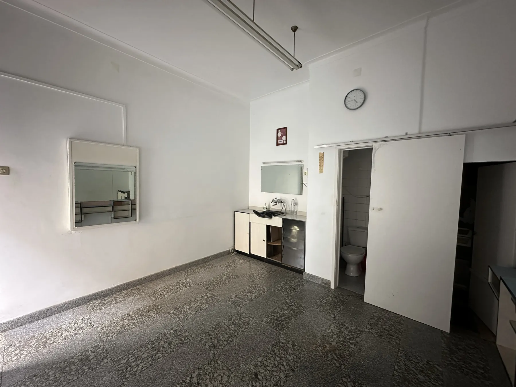 O salão visto da entrada antes da obra, com espelho de parede, bancada de lavatório e porta do lavabo