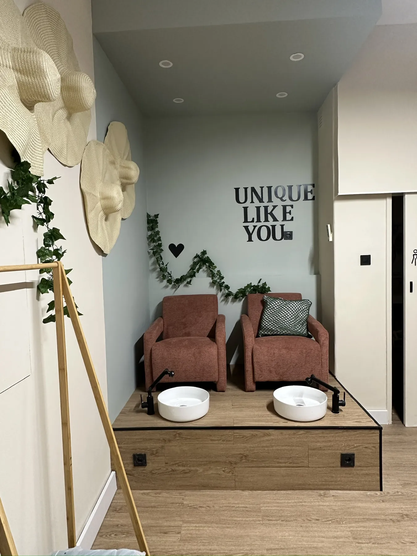 O canto da pedicure concluído, com poltronas terracota, lavatórios e chapéus de palha na parede